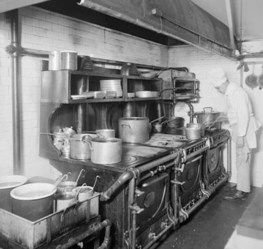 A man standing in front of an old fashioned stove.