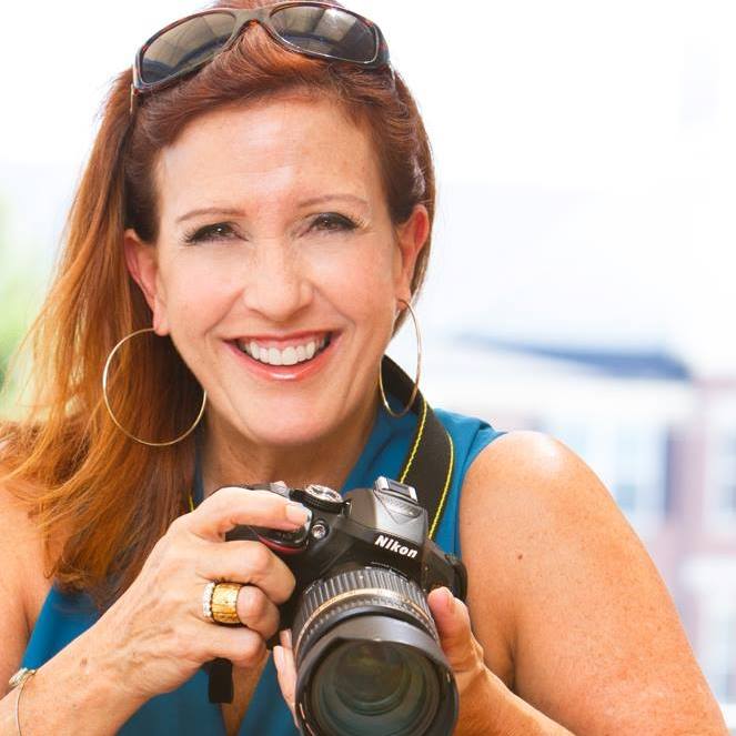 Smiling woman holding a camera outdoors.