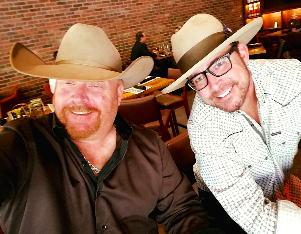 Two men wearing hats and smiling for a picture.