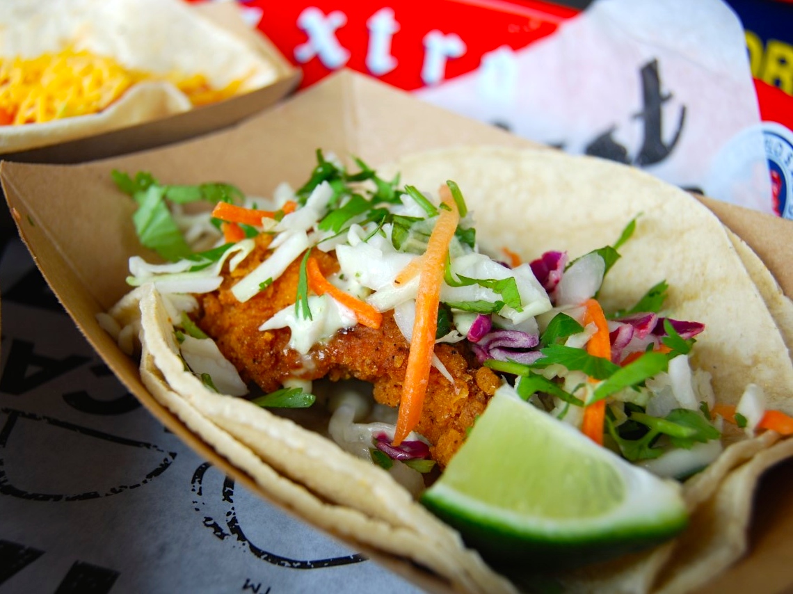 A taco with lettuce, carrots and lime wedges.