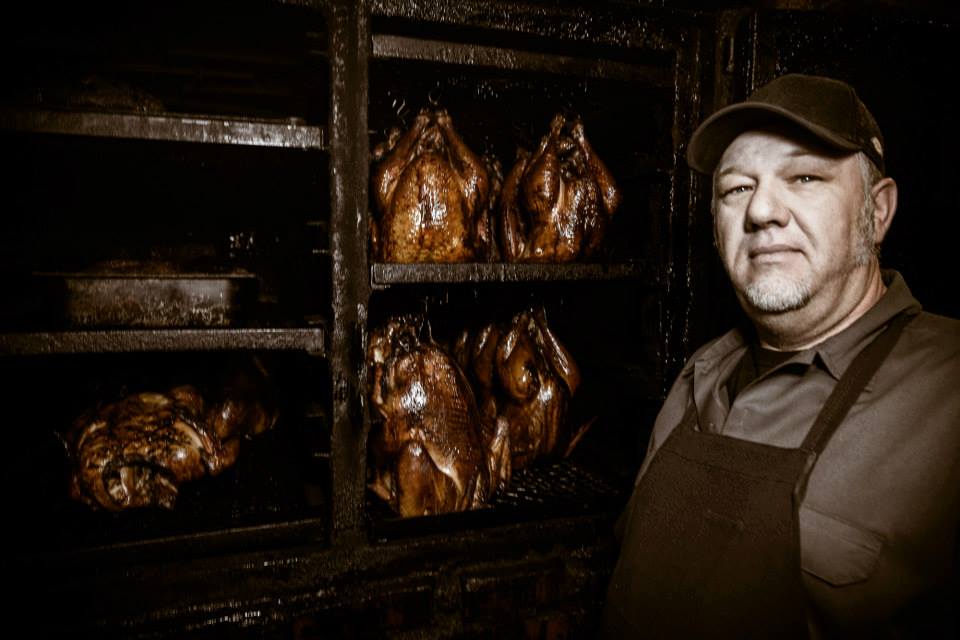 A man standing in front of several racks filled with meat.