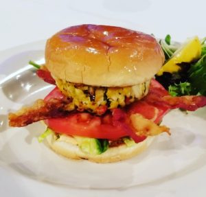 A burger with bacon and tomato on top of it.