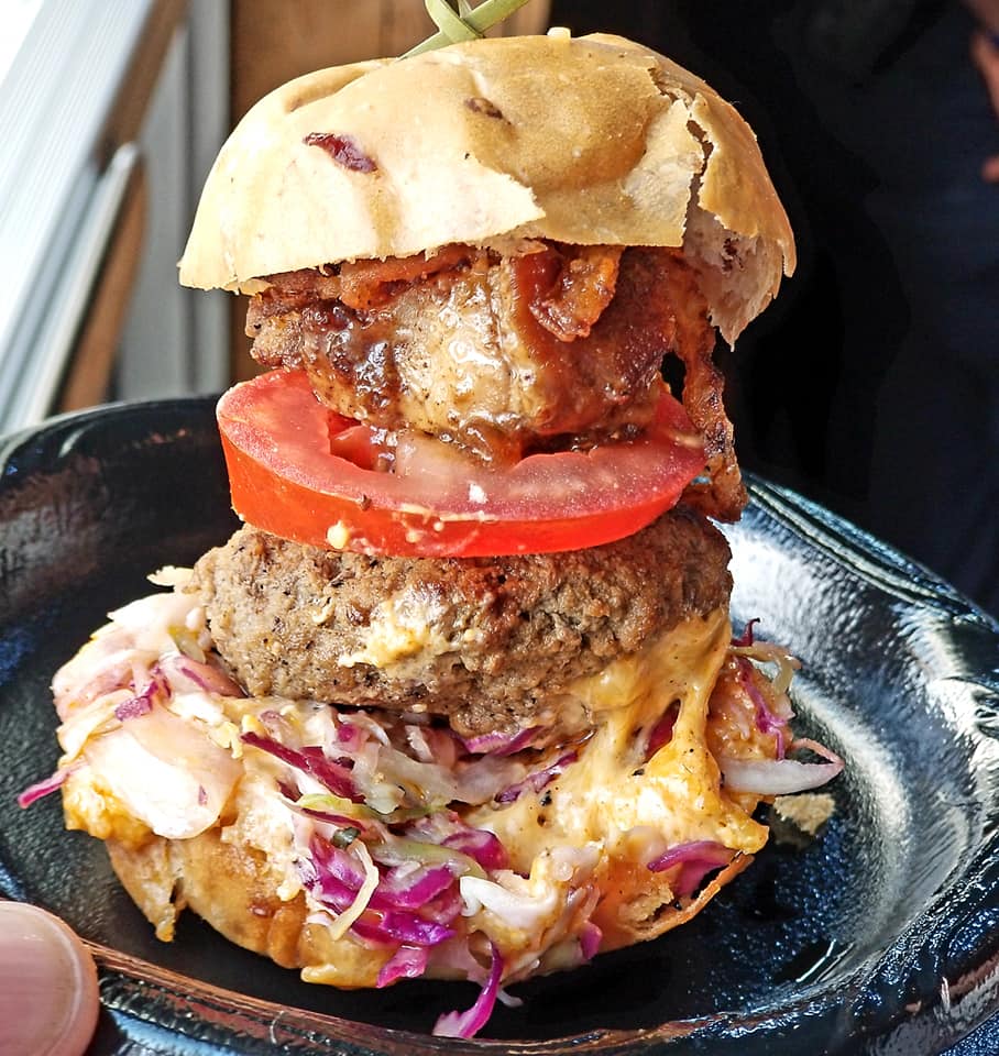 A hamburger with meat, tomato and coleslaw on top.