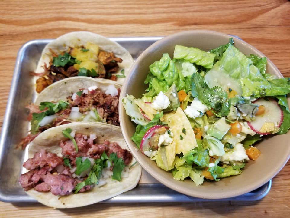 A tray with three tacos and salad on it.