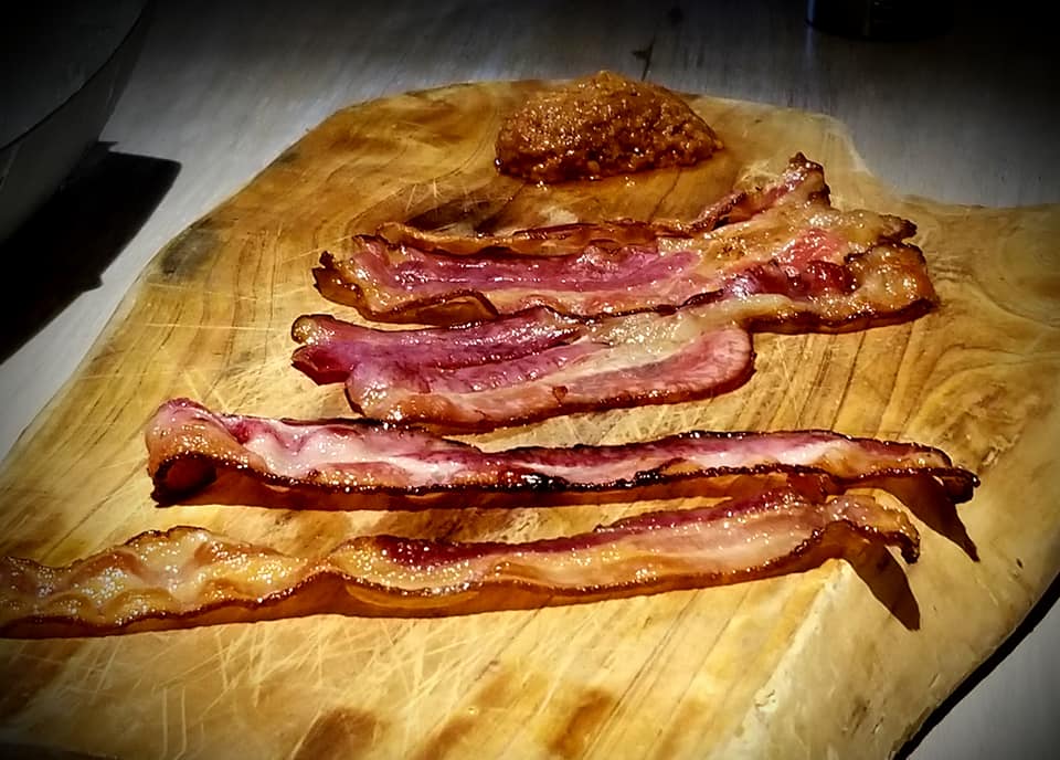 A wooden cutting board with bacon on it.