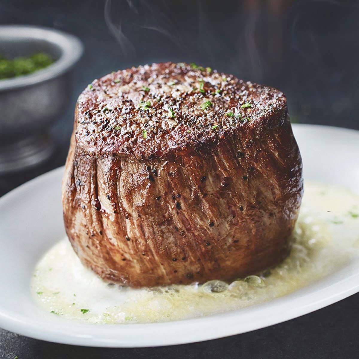 A steak on top of a white plate with sauce.