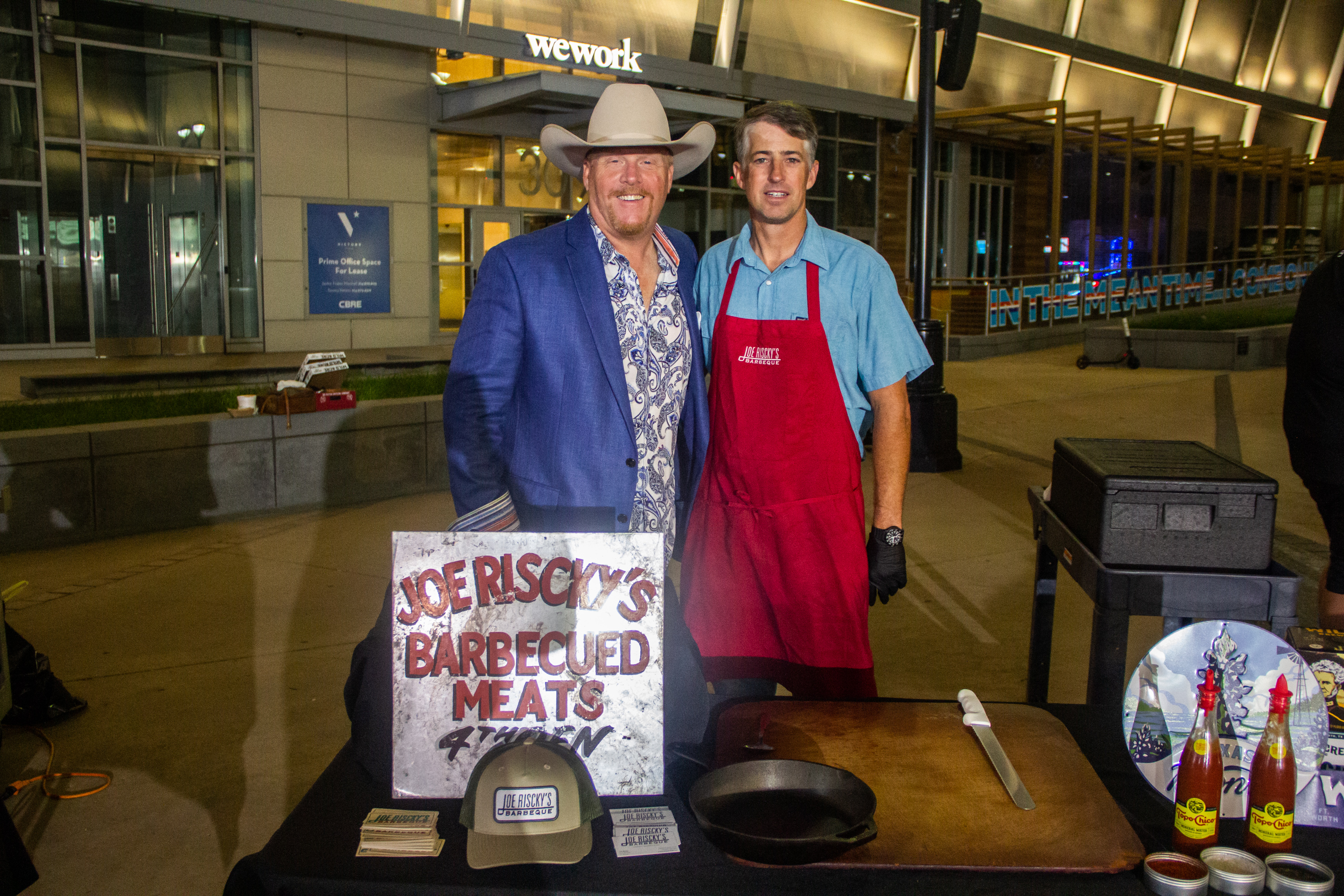 Two men standing next to a table with meat on it.