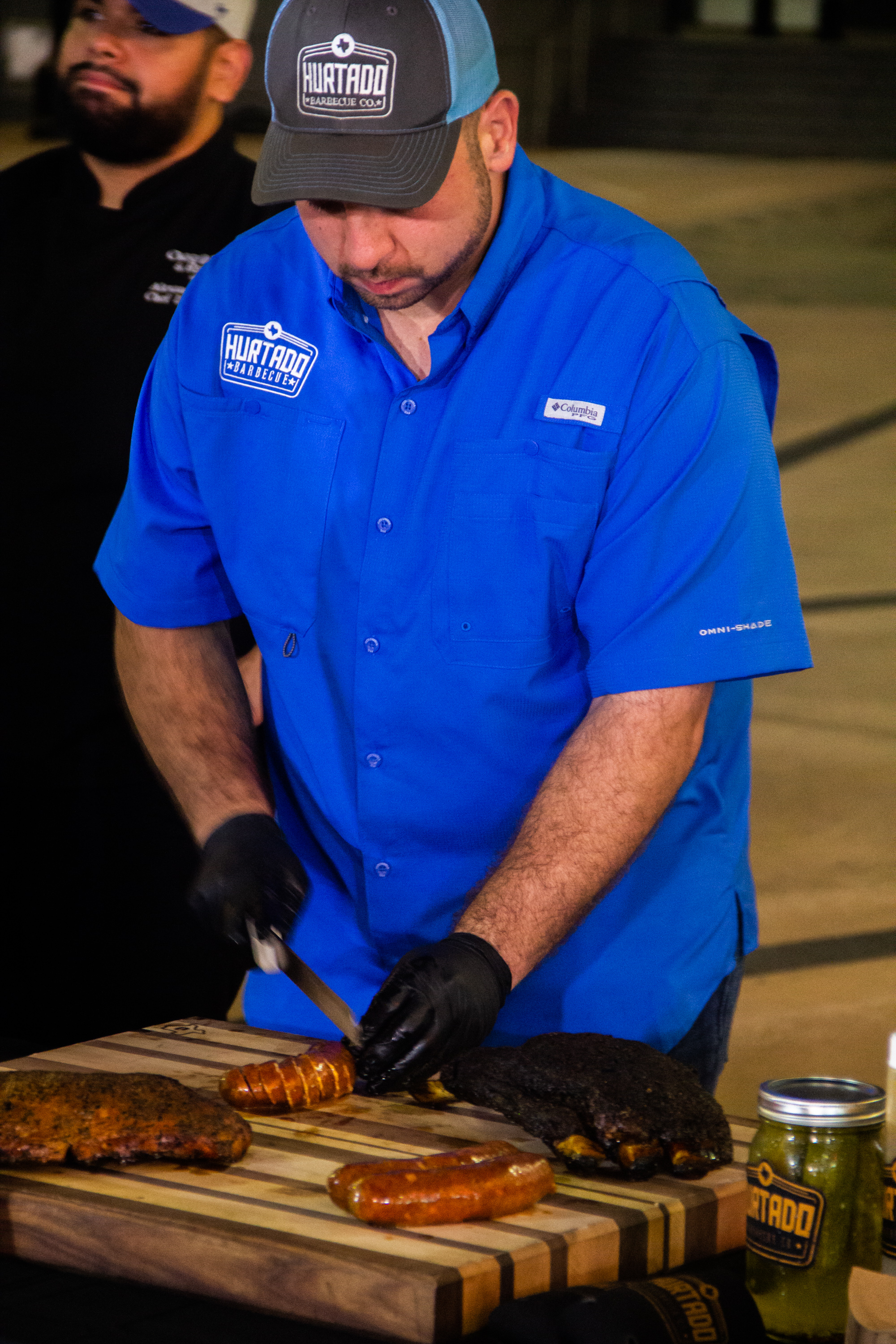 A man in blue shirt cutting food on top of grill.