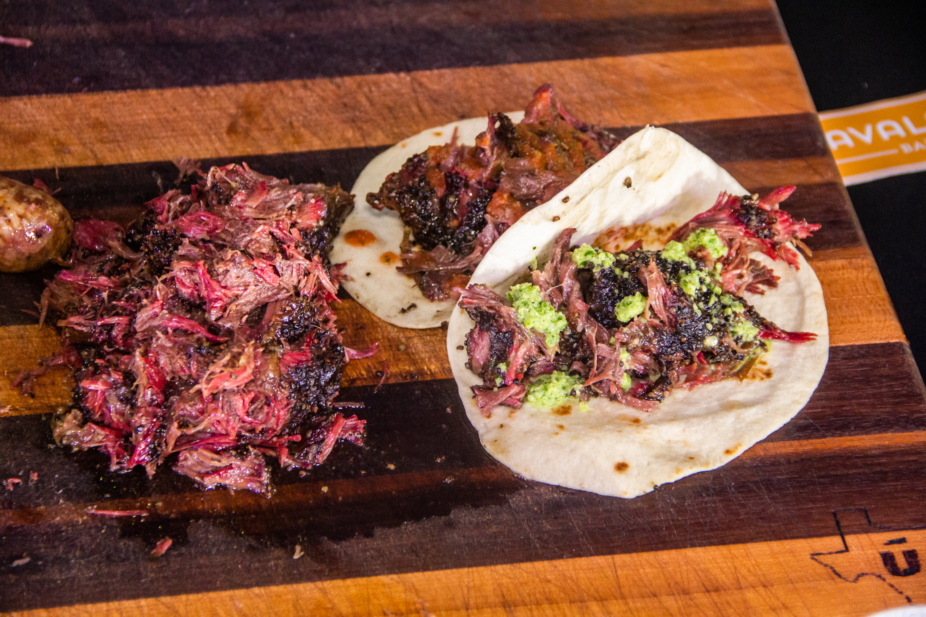 A wooden table with two tacos and some meat.