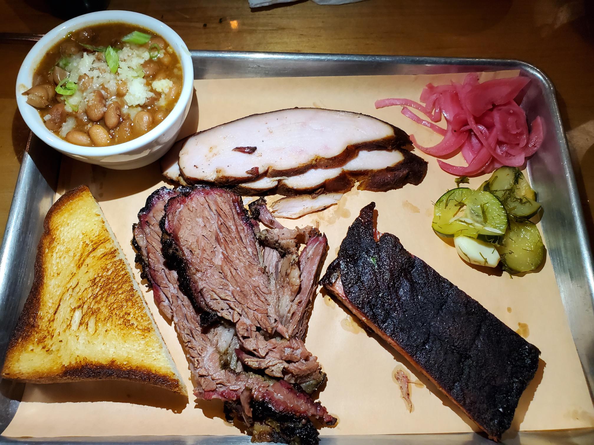 A tray of food with meat, bread and pickles.