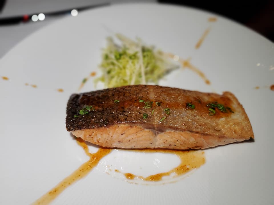 A piece of fish is on the plate with some sauce.