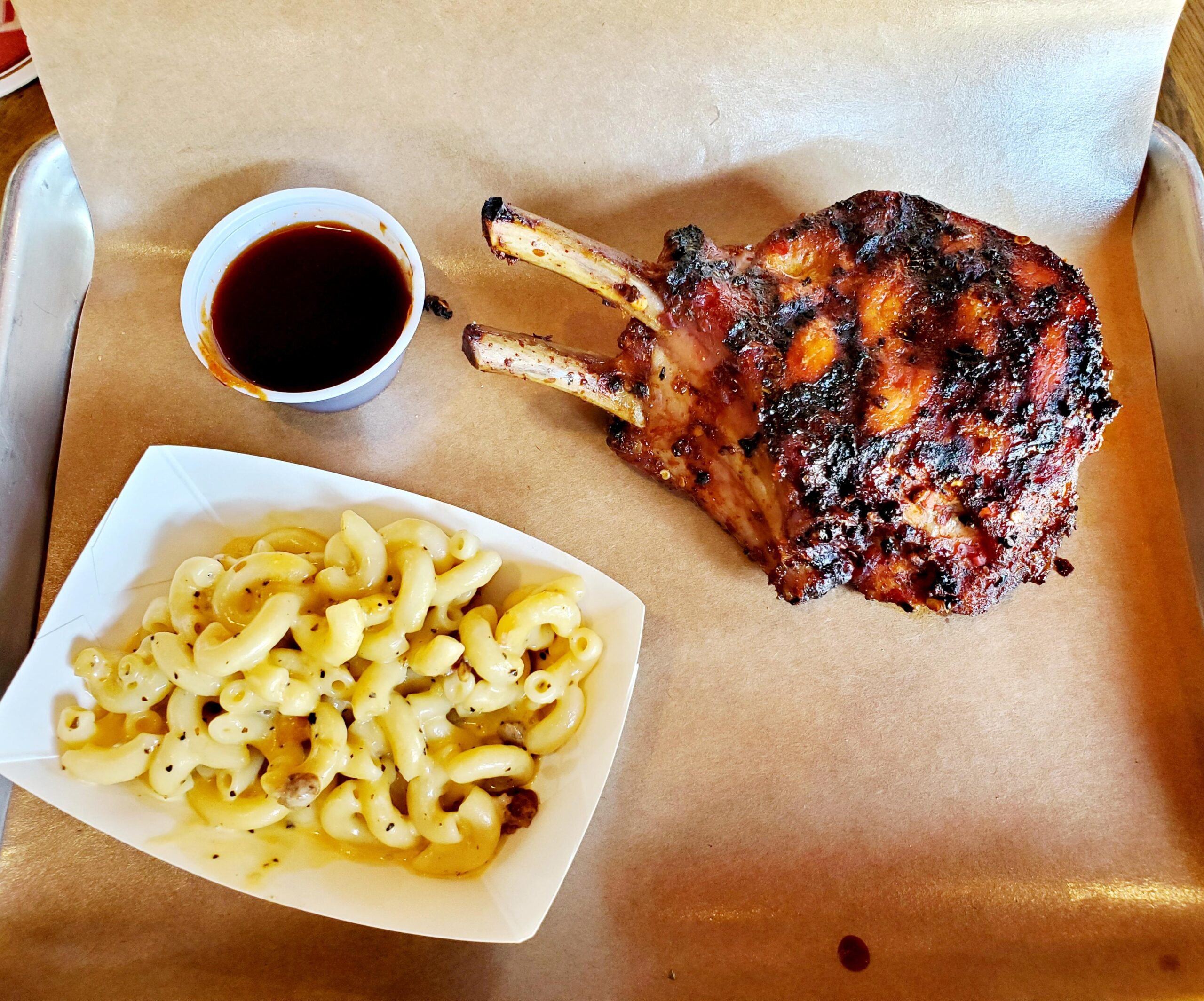 A table with macaroni and cheese, grilled pork chop and sauce.