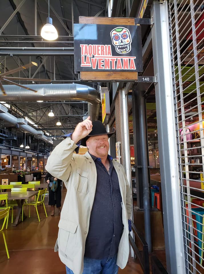 A man in a hat and jacket standing next to a store.