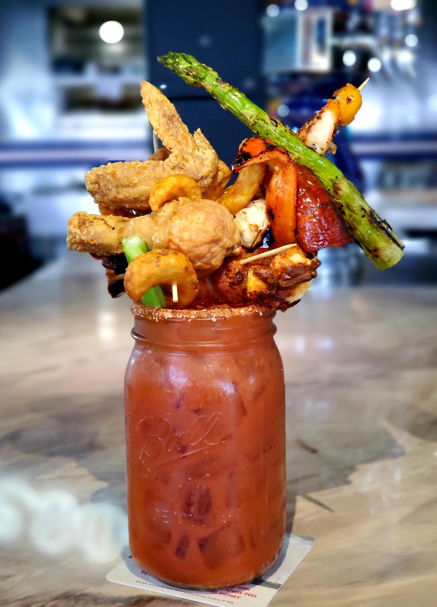 A bloody mary with some veggies and bacon on top of it.