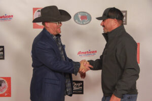 Two men shaking hands on a red carpet.