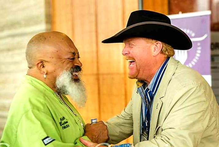 Two men are laughing together while one of them is wearing a cowboy hat.