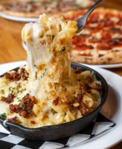 A plate of macaroni and cheese with some pizza on the side.