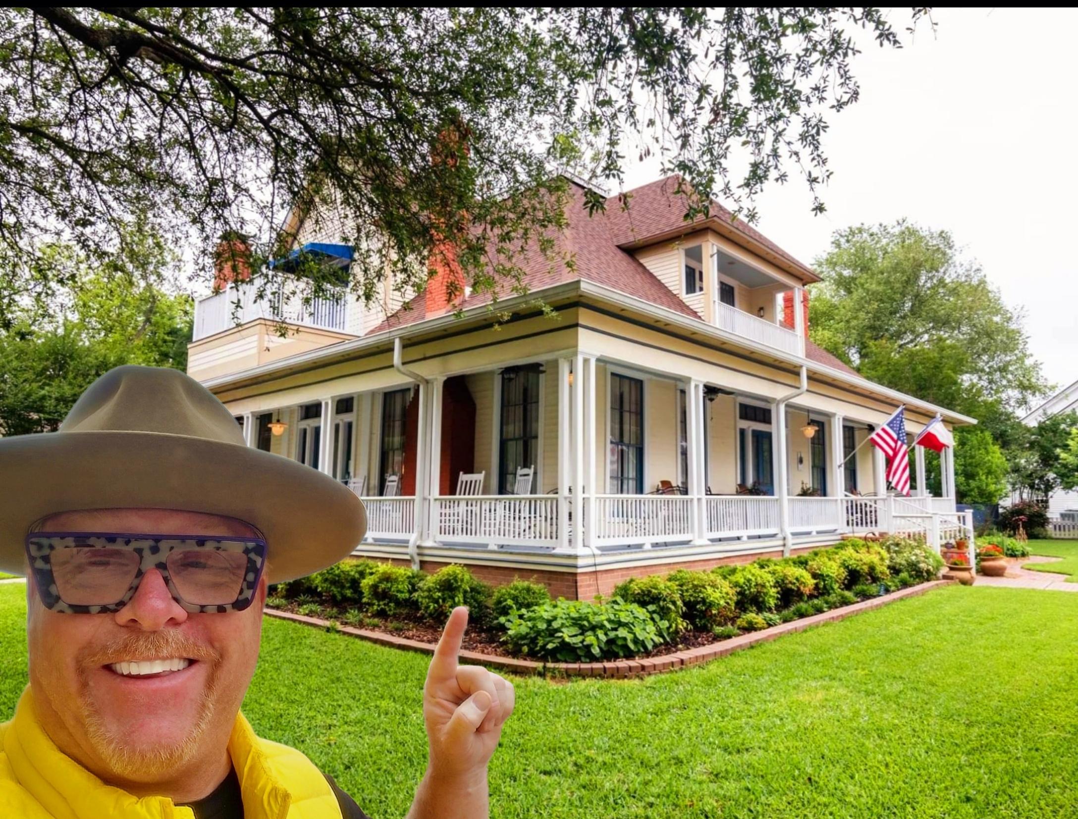 A man in a hat and sunglasses standing outside of a house.