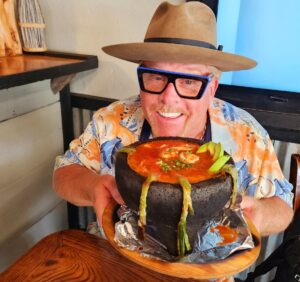 A man holding a large cake with a hat on.