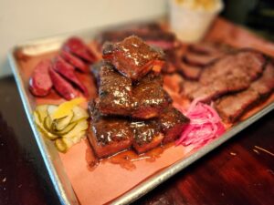 A tray of meat and pickles on top of a table.