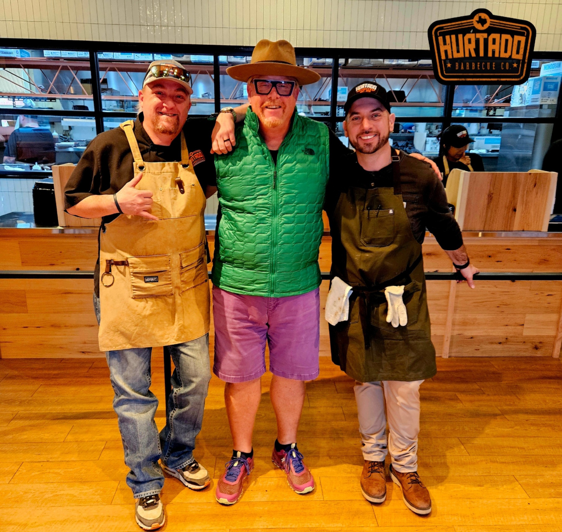 Three men standing in a room with aprons on.